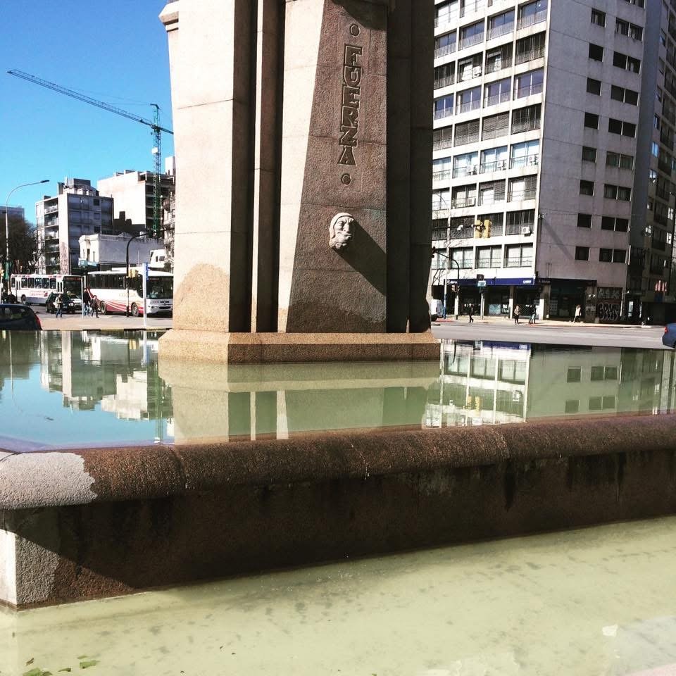 Base del Obelisco de Montevideo con la palabra Fuerza grabada en la piedra, reflejada en el agua de la fuente.